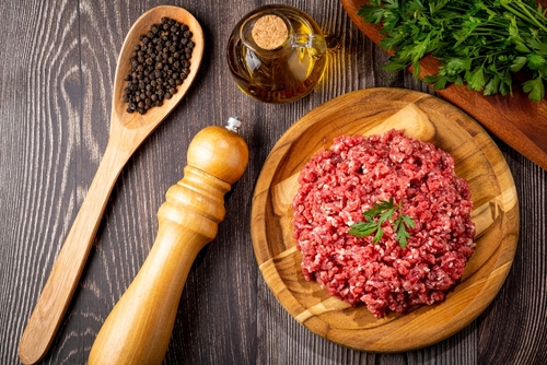 carne moída em um prato de madeira com ingredientes em volta - cortes de carne - Assaí Atacadista