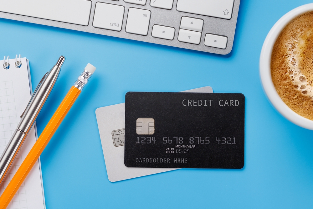 cartão de crédito fictício em um fundo azul com outros itens - decisões financeiras - Assaí Atacadista