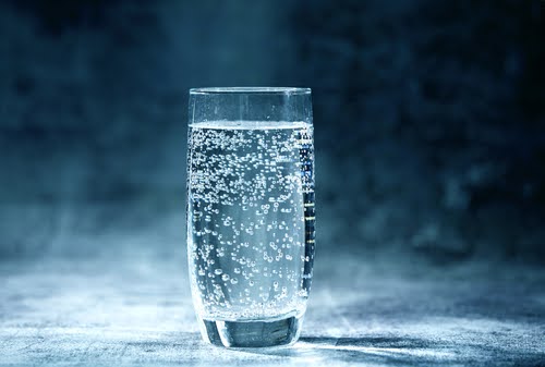 copo transparente com água com gás em um fundo azul - hidratação no verão - Assaí Atacadista