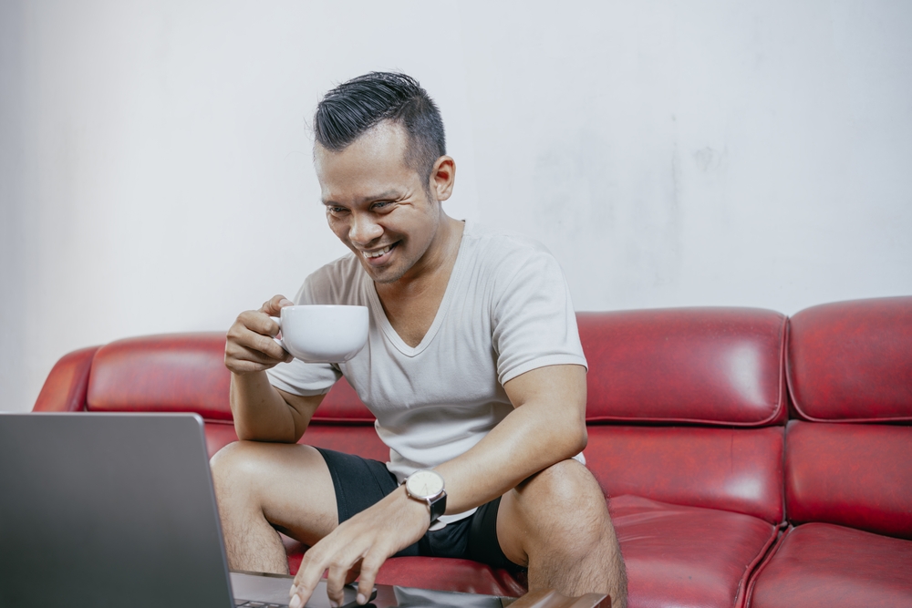 homem asiático em um sofá vermelho com xícara de café na mão - Assaí Atacadista - piloto automático