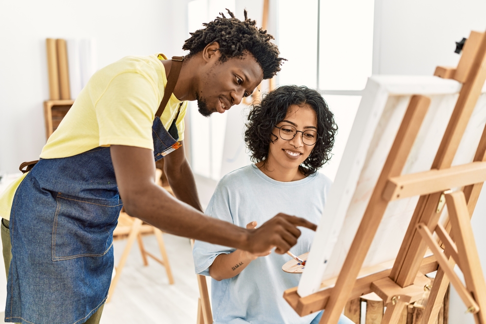 jovem professor de artes negro ensinando mulher aluna a pintar - monetizar hobbys - Assaí Atacadista