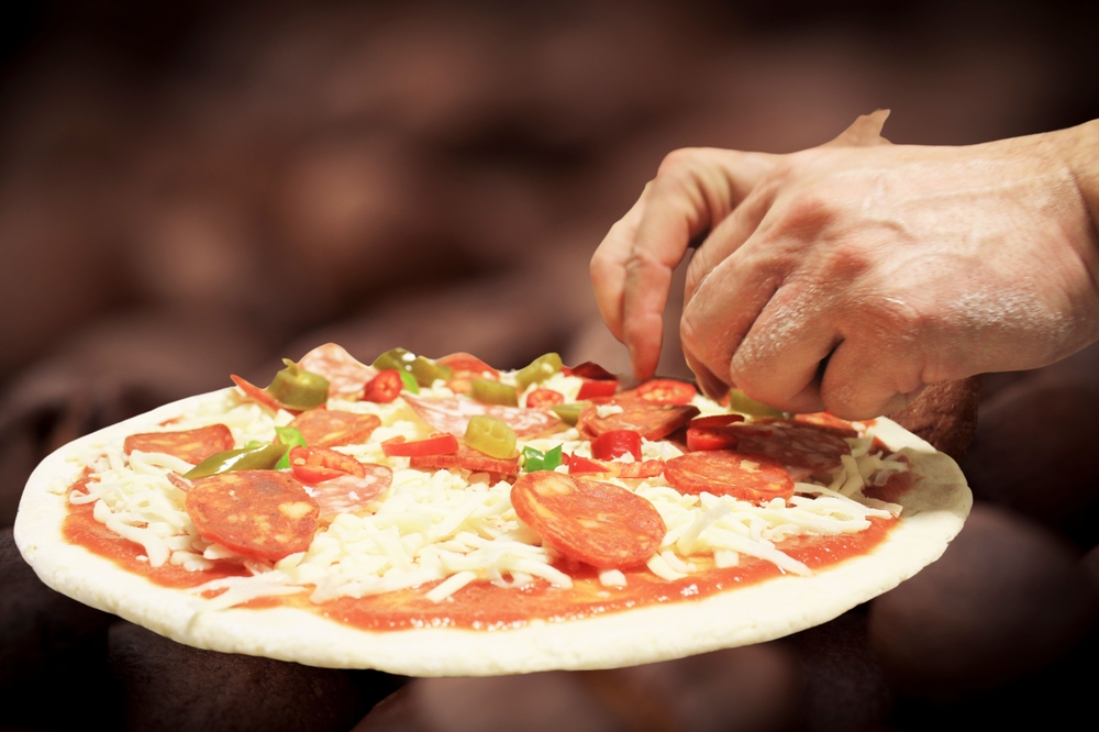 mãos brancas colocando ingredientes em uma pizza - comércios transformadores - Assaí Atacadista