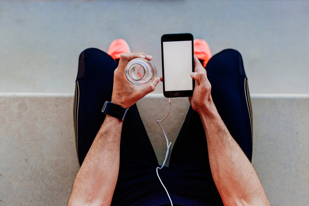 mãos brancas masculinas segurando uma garrafa de água e um celular - tecnologia para economizar - Assaí Atacadista