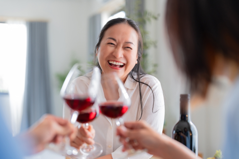 mulher asiatica sorrindo brindando com uma taça de vinho - bebidas para presentear - Assaí Atacadista