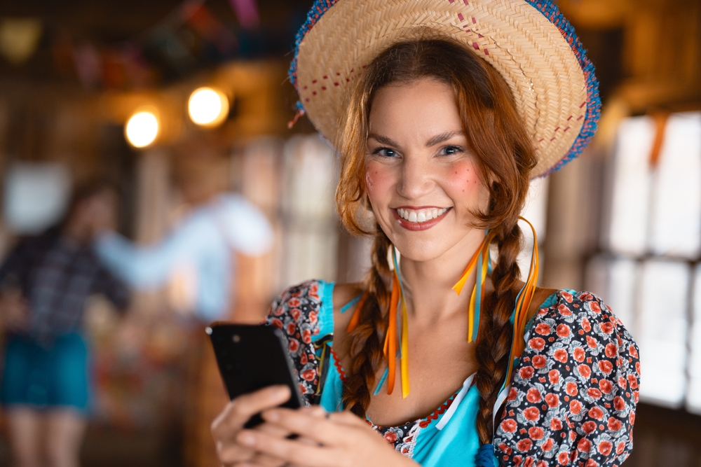 mulher branca com traje junino e celular na mão - São João empreendedor - Assaí Atacadista