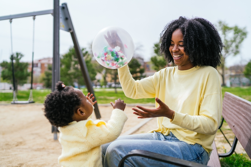 mulher negra mãe brincando com a filha bebê em um parque - lazer econômico - Assaí Atacadista