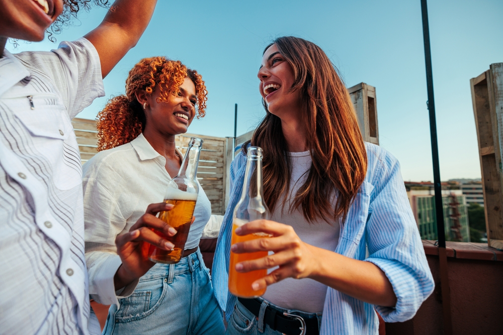 mulheres jovens felizes com uma garrafa de cerveja na mão - bebidas para presentear - Assaí Atacadista