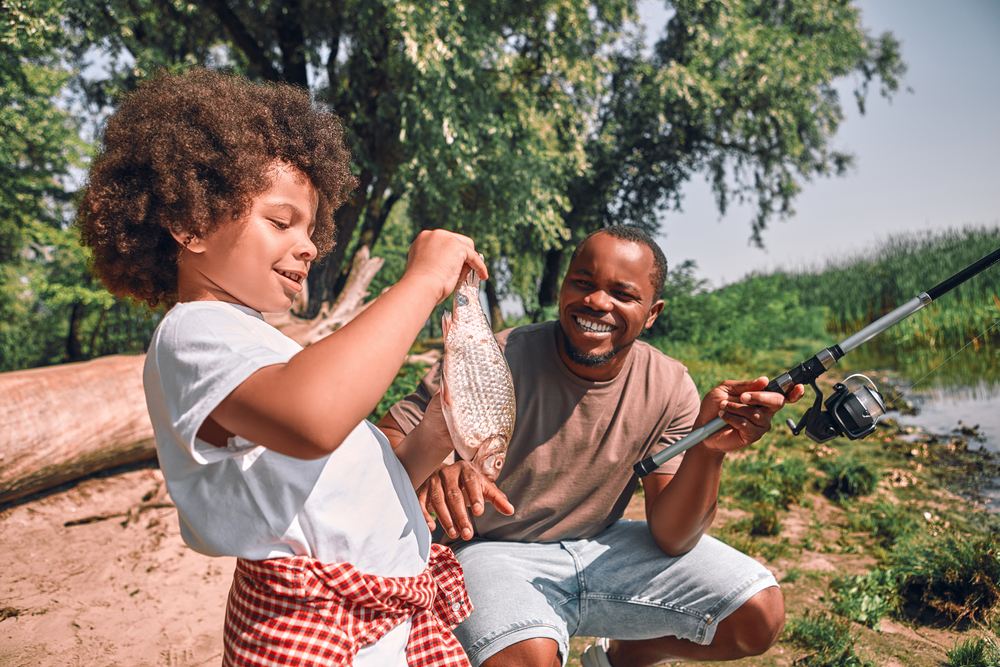 pai e filho pretos felizes pescando com peixe nas mãos - presentes para pais - Assaí Atacadista