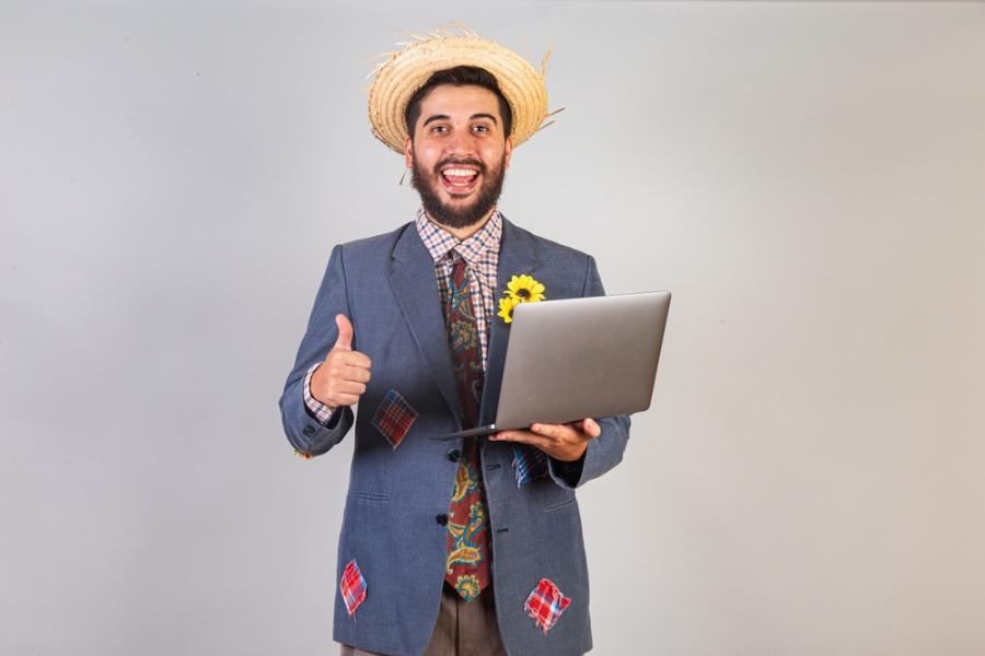 homem com traje de festa junina e notebook na mão - São João empreendedor - Assaí Atacadista