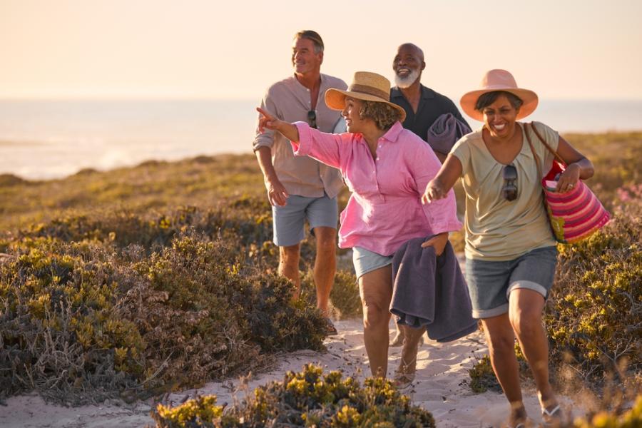 quatro pessoas felizes e diversas andando na areia segurando malas - piloto automatico - Assaí Atacadista