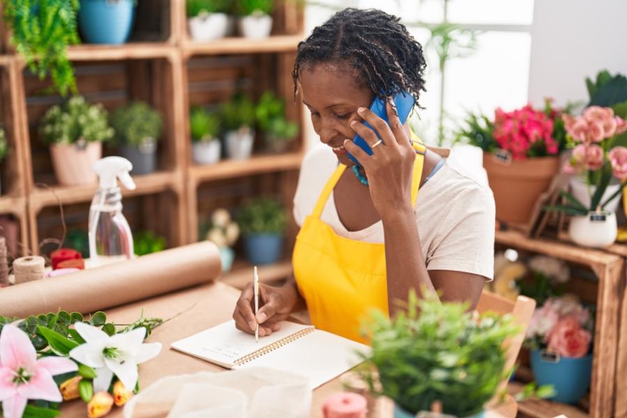 senhora negra empreendedora falando no celular em uma floricultura - sucesso do cliente - Assaí Atacadista