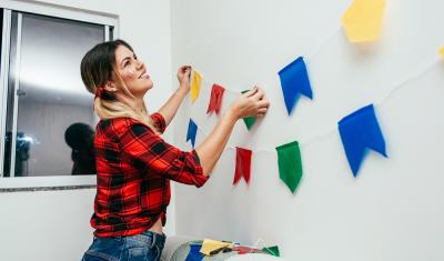 mulher branca colocando decoração de festa junina na parede - Assaí Atacadista