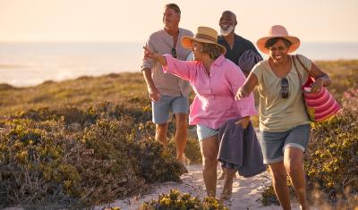 quatro pessoas felizes e diversas andando na areia segurando malas - piloto automatico - Assaí Atacadista