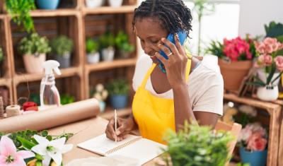 senhora negra empreendedora falando no celular em uma floricultura - sucesso do cliente - Assaí Atacadista